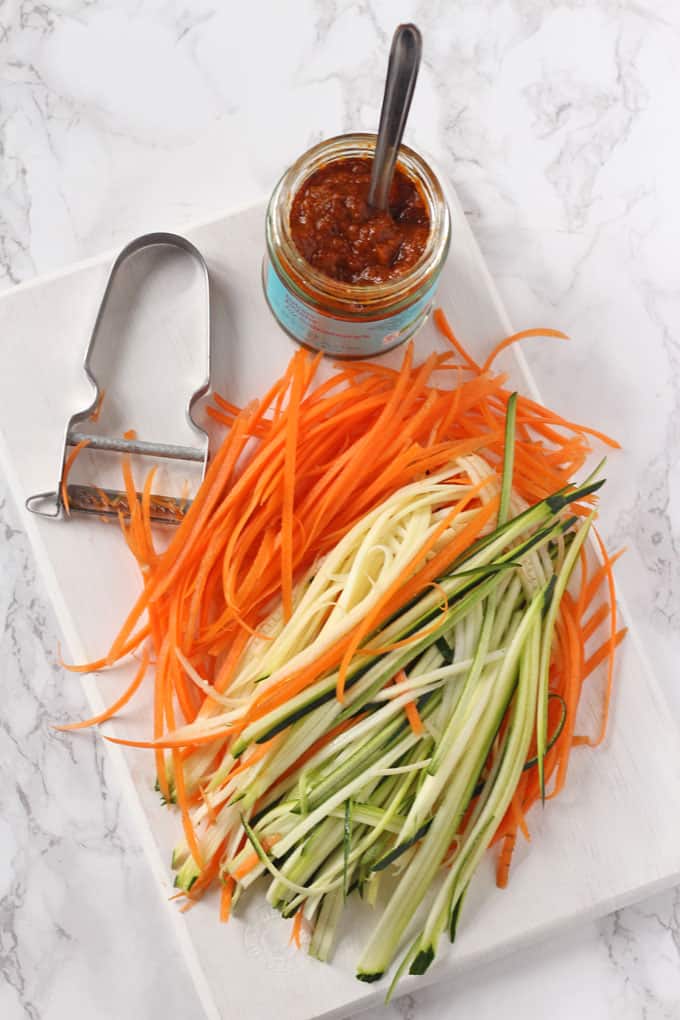 julienne carrots and courgette on a chopping board with a jar of laksa paste