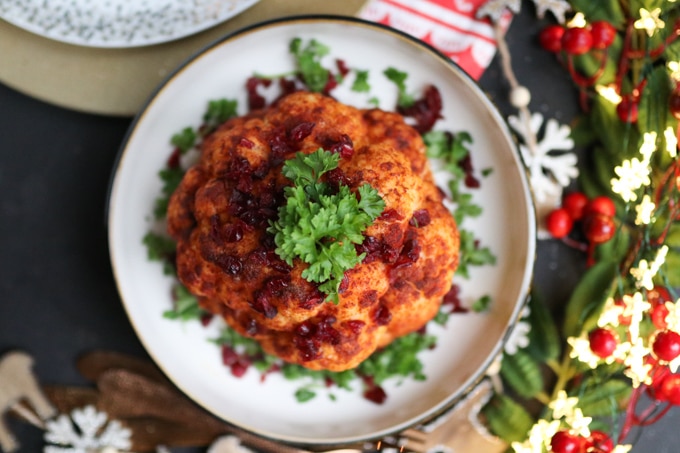 Whole roasted cauliflower with hazelnut pesto on a white serving plate on a festively decorated table