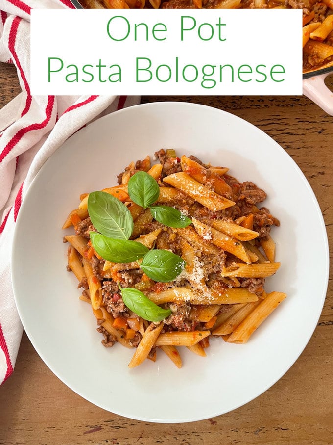One pot past bolognese served in a large white pasta bowl, and garnished with grated Parmesan cheese and basil leaves.