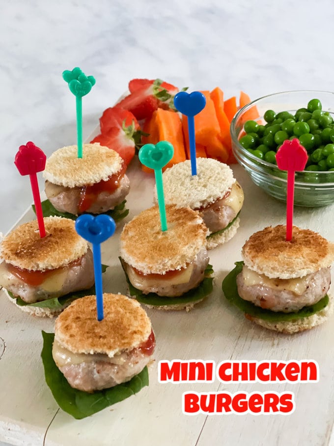 Mini Chicken burgers served on a plate and being held together with Bright and colorful Pick Stick, served alongside a bowl of garden peas and fresh veggies.
