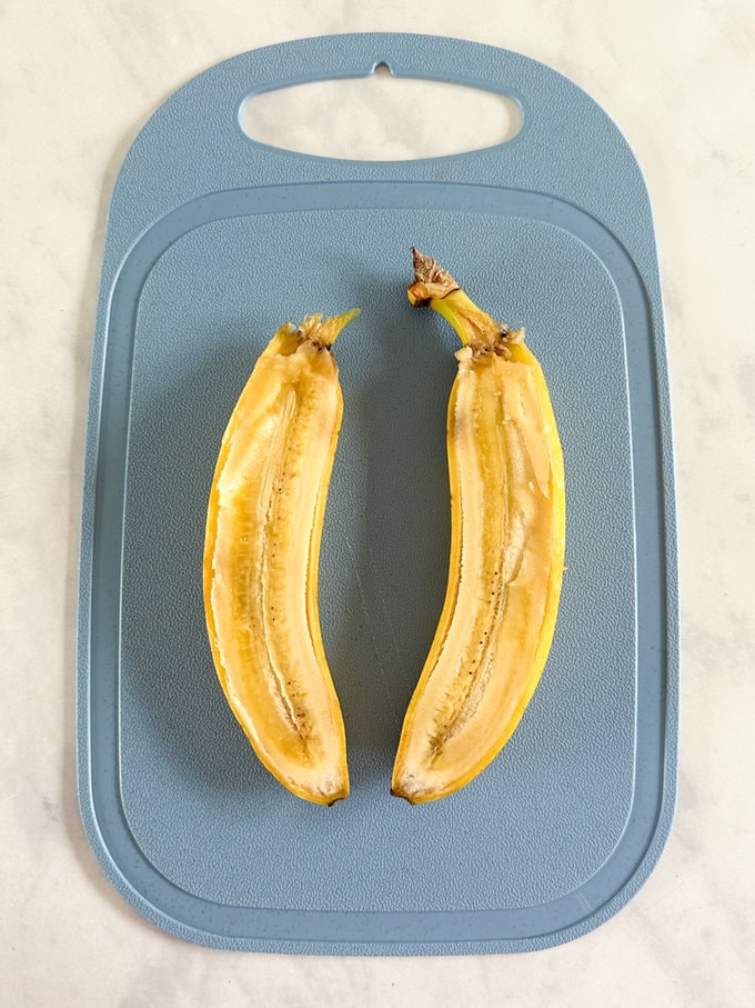 Raw banana cut in half length ways on a blue chopping board.