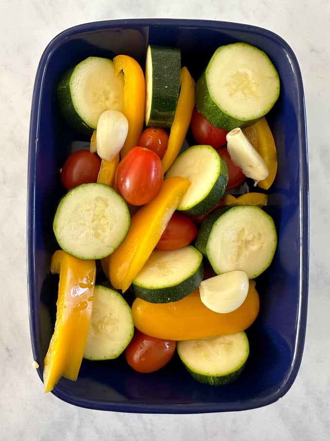 Bright veggies chopped and arranged in a blue oven dish.