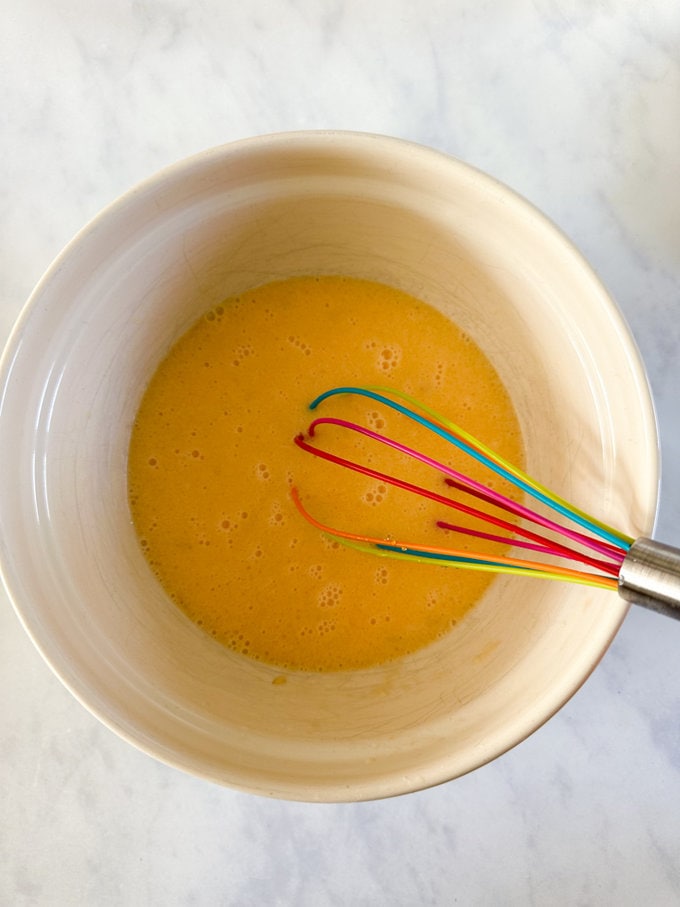 Ingredients being mixed together in a bowl with a colorful whisk. 