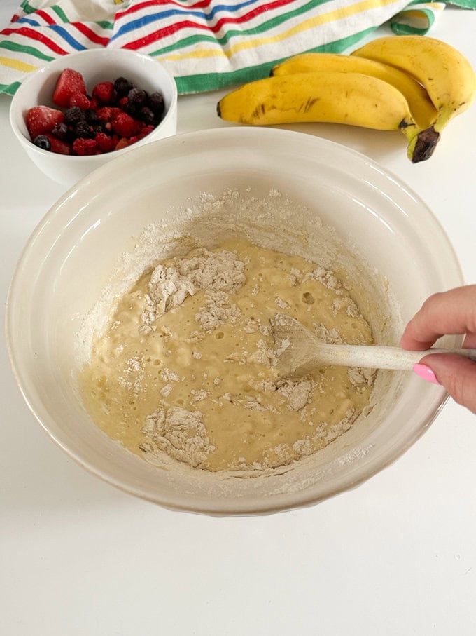 Ingredients for the breakfast cake being combined in a large mixing bowl with a wooden spoon.