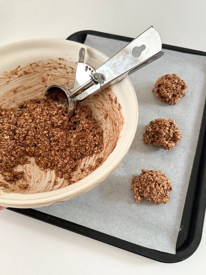Nutella Breakfast Cookies mix in a bowl and being portioned out onto a baking tray using a ice cream scoop.