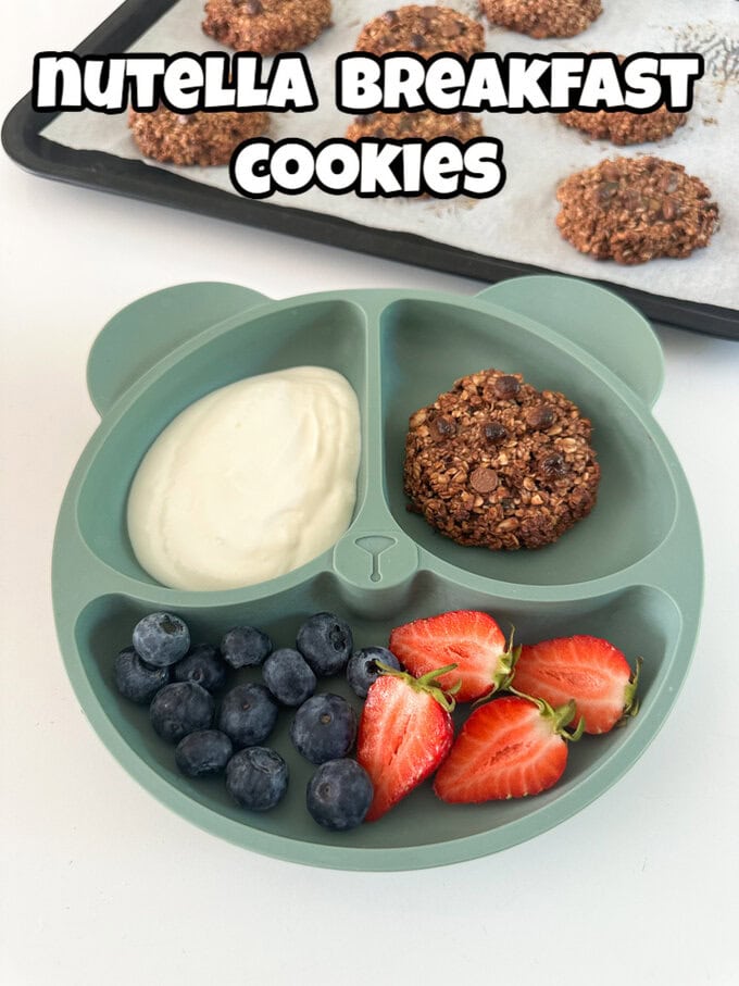 A Nutella Breakfast Cookie served on a bear face shaped divided plate with a portion of greek yogurt and fresh strawberries and blueberries.