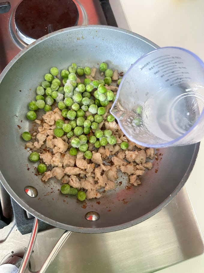 Frozen peas being added to the cooked sausage meat.