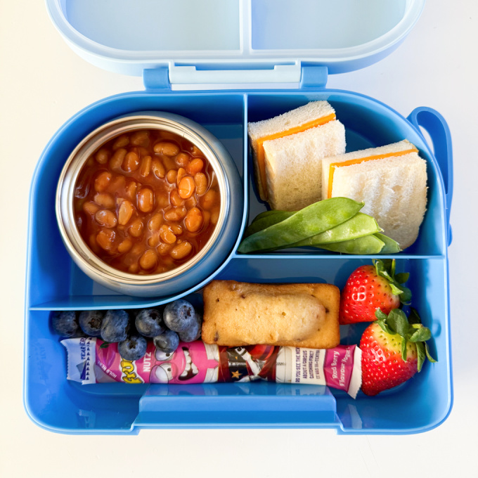 Baked beans in a thermos pot served with a cheese sandwich and other treats.