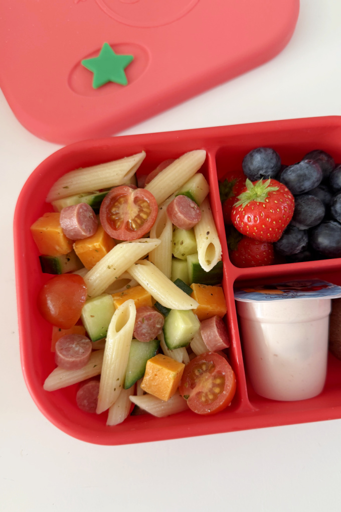 5 Minute Lunchbox Pasta Salad served in a bright red lunch box with fresh berries, yogurt and a sweet treat.
